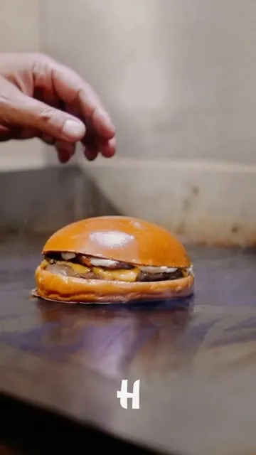 Mão finalizando um burger na chapa, em publicação da Hicks